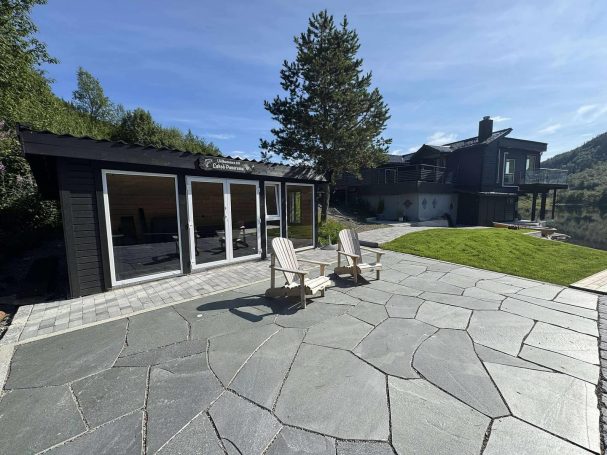 Modern trädgård med stentrappa, två stolar och en svart byggnad i bakgrunden.