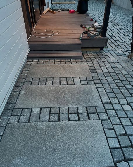 Stenlagd gång med plattor som leder till en trädäckad entré.