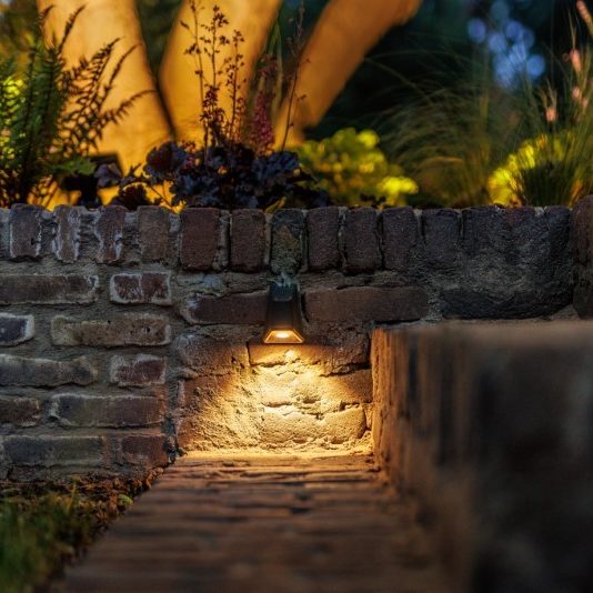 Lågspänningsbelysning utomhus längs mur och gång i trädgårdsmiljö